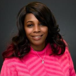Woman wearing a pink sweater, smiling, with dark hair, a necklace, against a gray background.