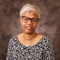 Man in glasses, smiling, wearing a black blazer, white shirt, orange boutonniere, and pocket square.