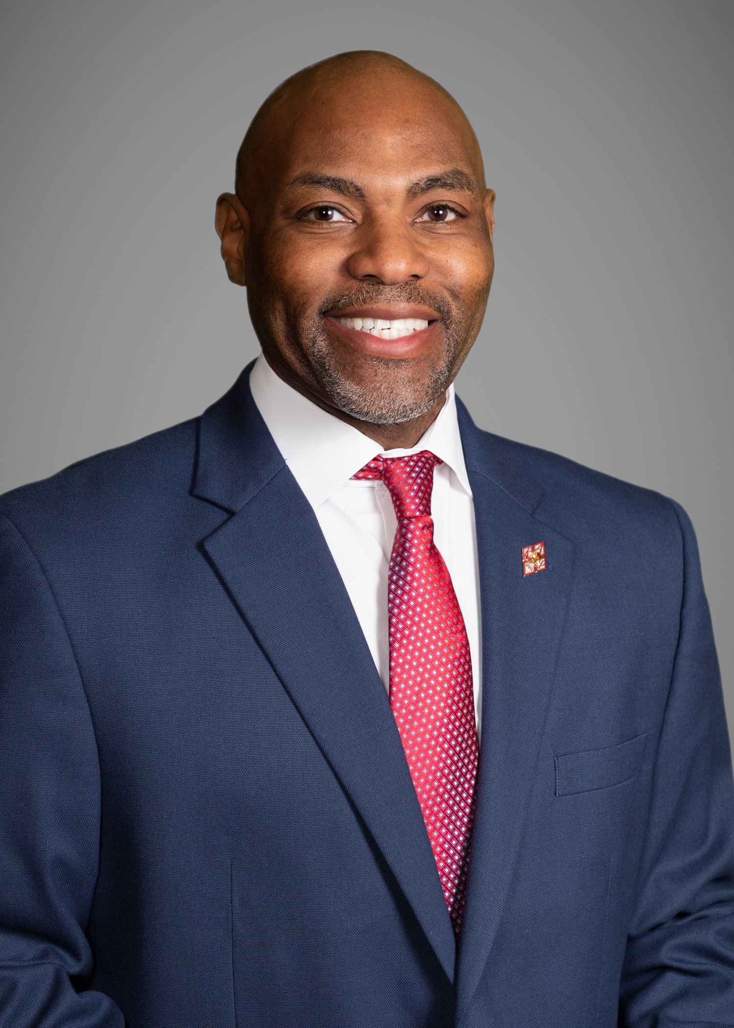 Man in a suit smiles at the camera, wearing a green and blue striped tie.