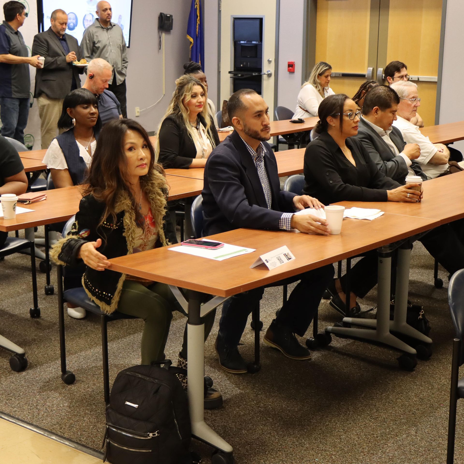 People seated at tables in a conference room, listening to a presentation.