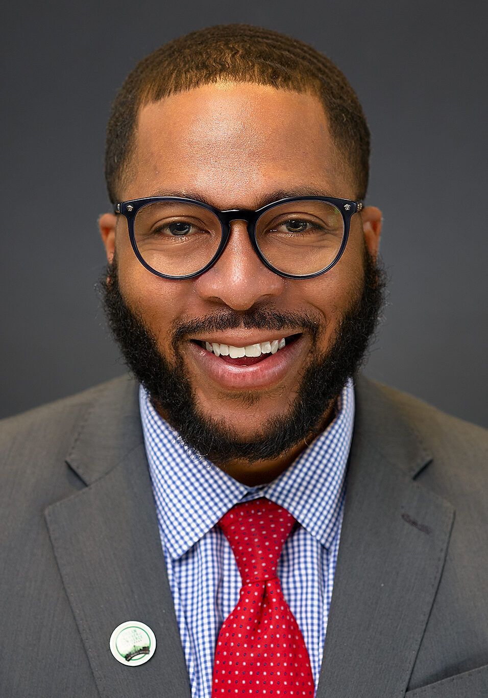Man with glasses, beard, and red tie smiling in a suit.