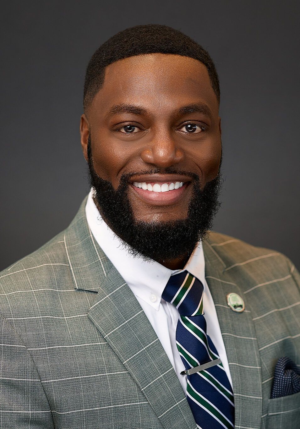 Man in a suit smiles at the camera, wearing a green and blue striped tie.