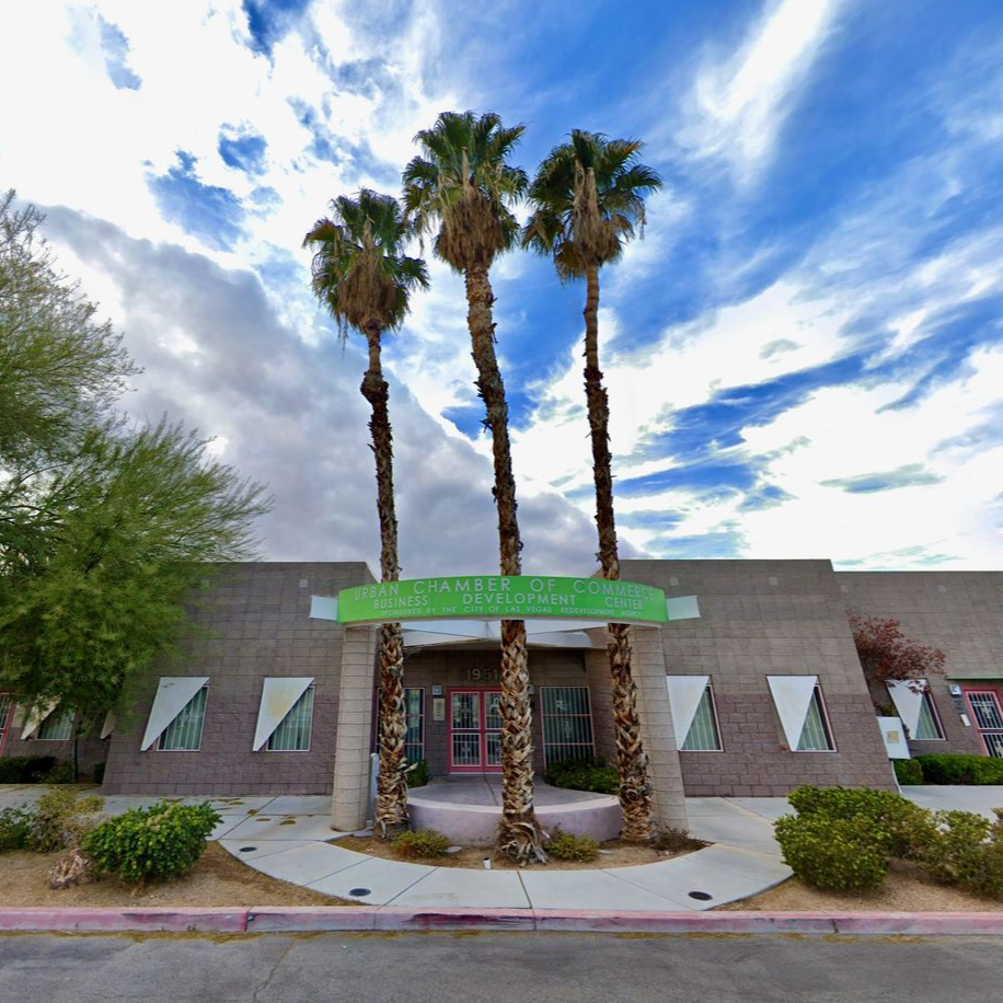 Building with three palm trees in front, under a cloudy sky.