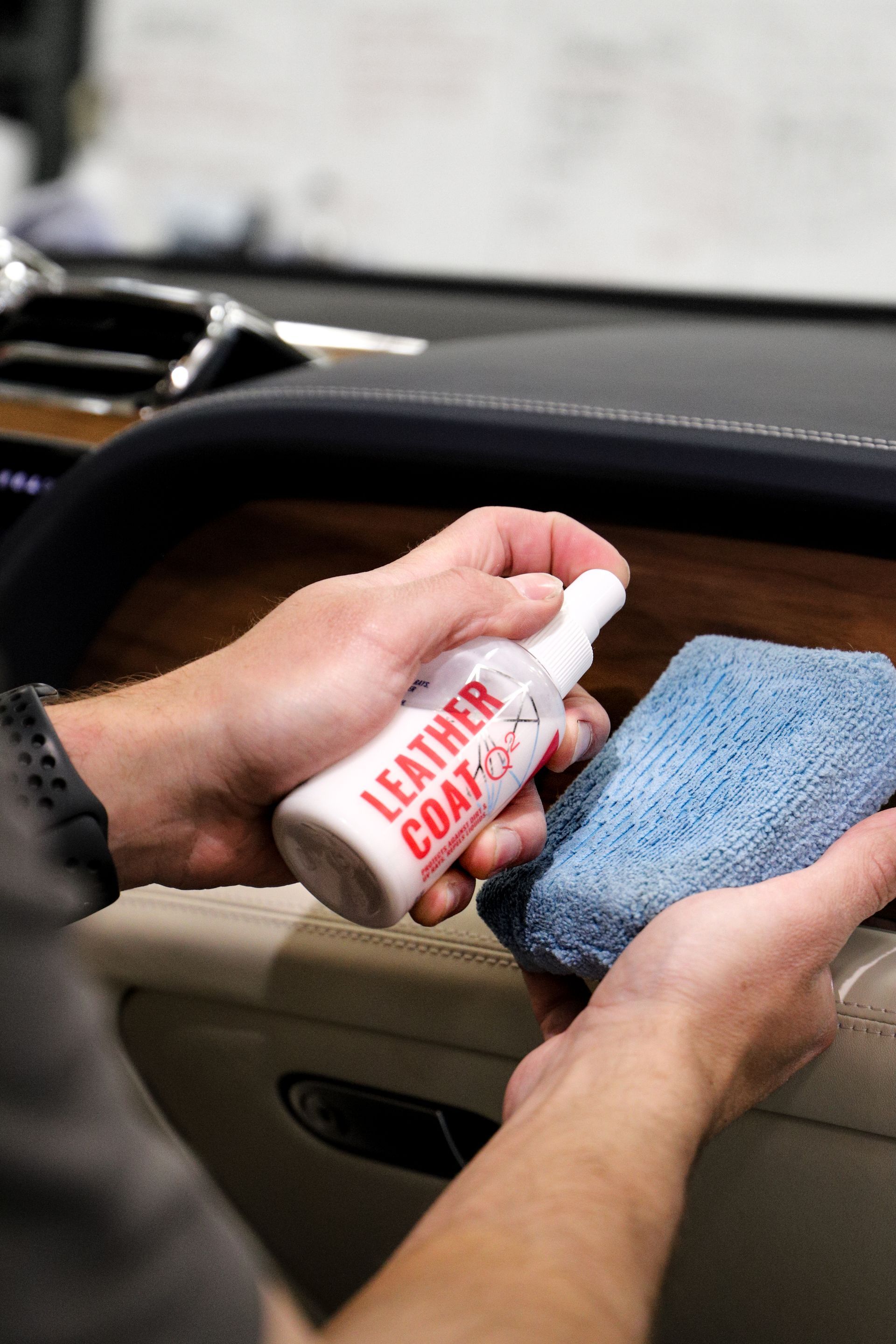 A person is holding a bottle of leather coat and a sponge.