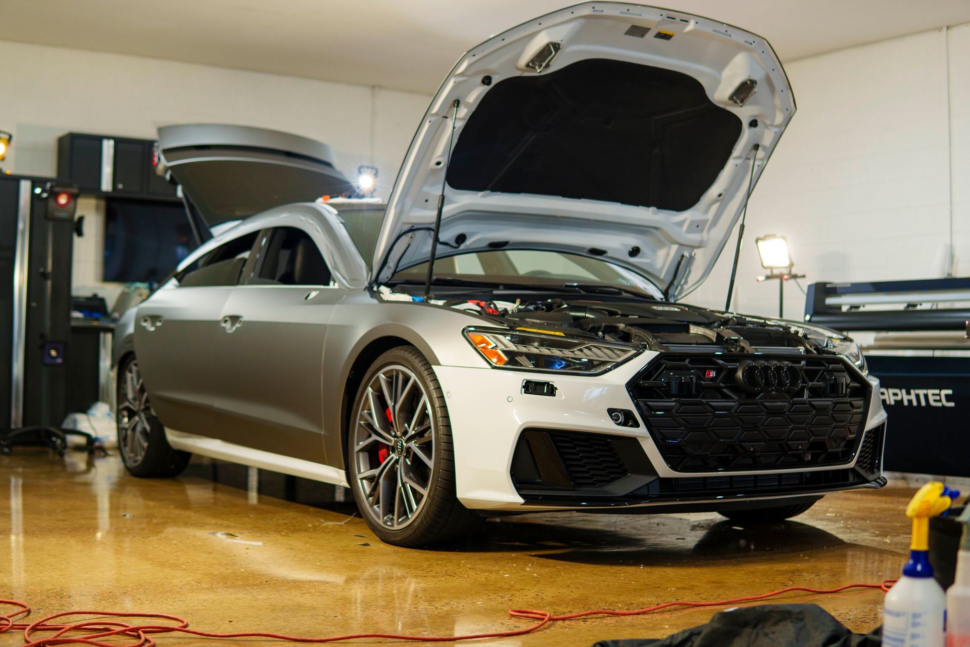 A car with the hood open is parked in a garage.