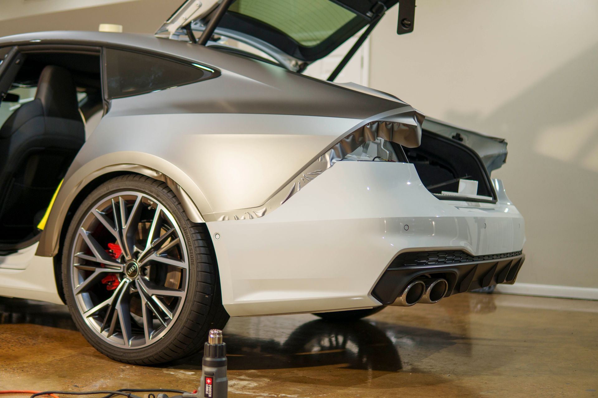 A white sports car with the trunk open is sitting in a garage.