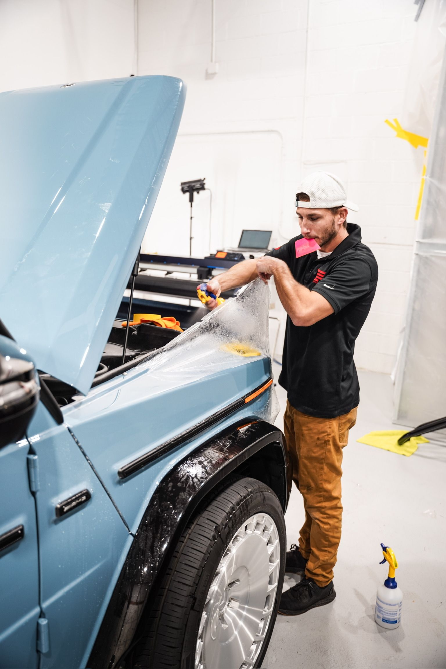 A man is standing next to a blue car with the hood open.