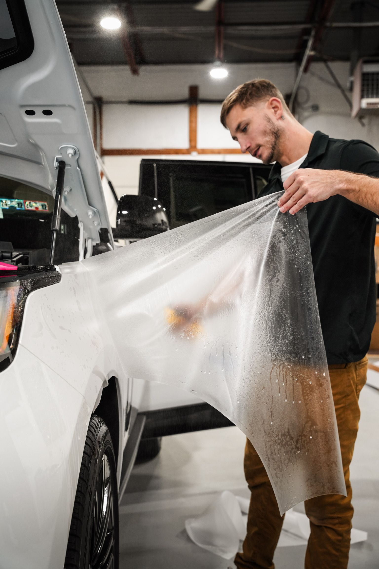 A man is wrapping a white truck with a clear plastic sheet.