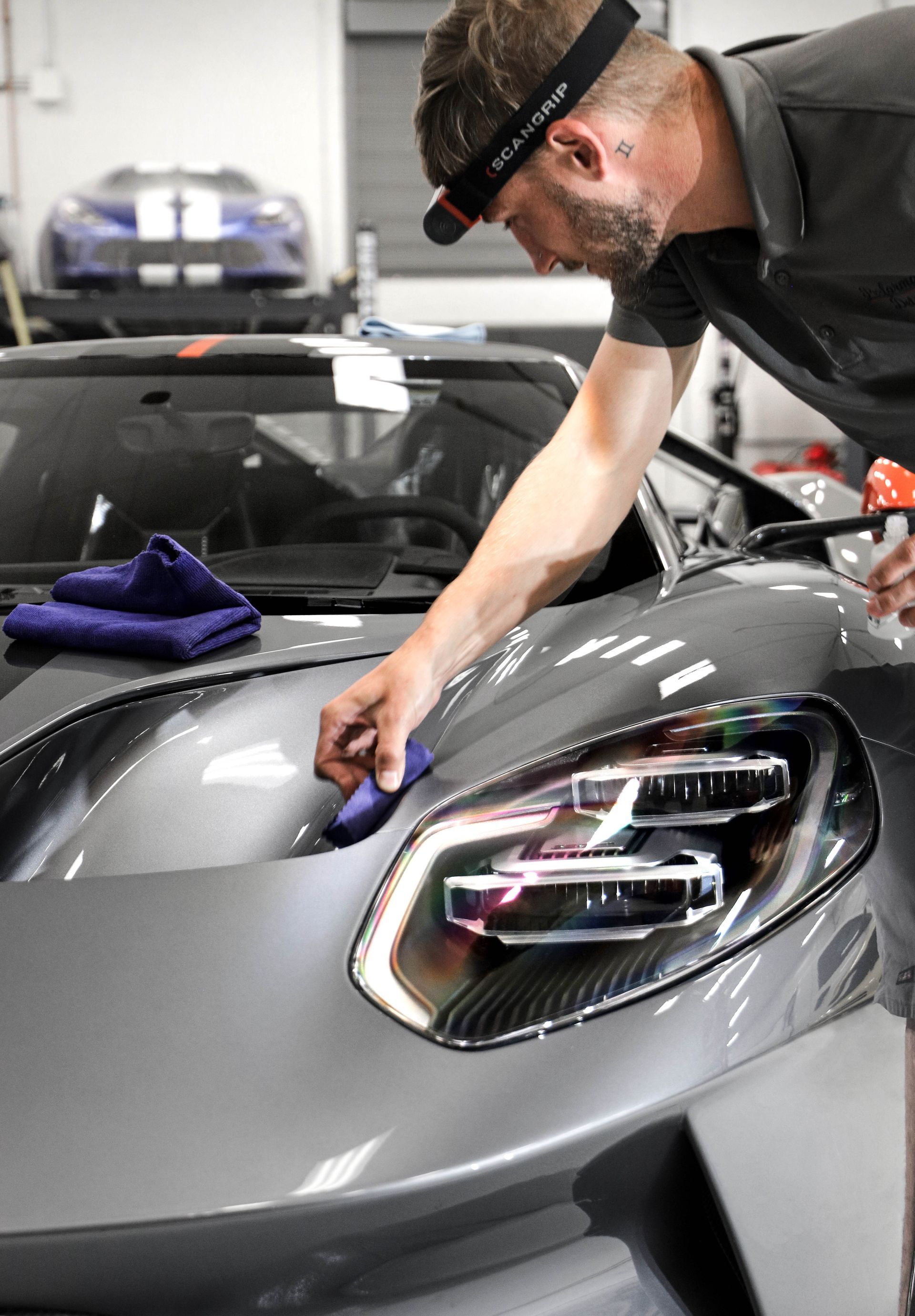 A man is cleaning the hood of a car in a garage.