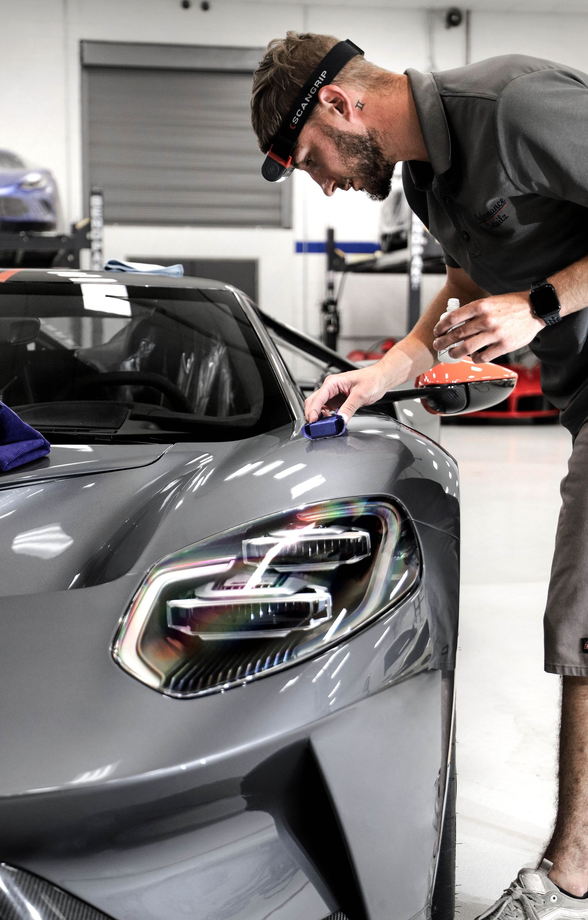 A man is working on a gray sports car in a garage.