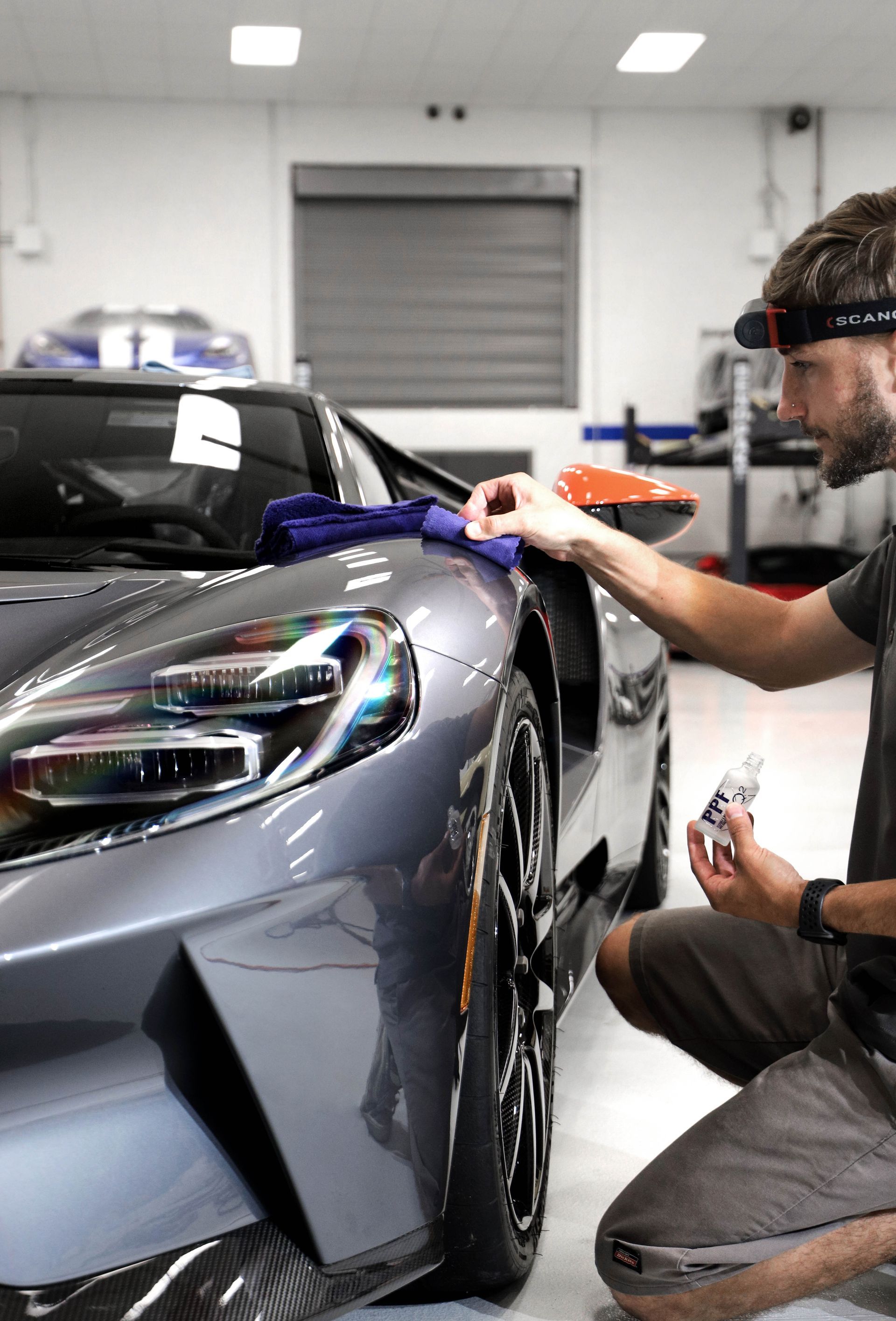 Man cleaning a gray sports car in a garage. He's holding a cloth and spray bottle.
