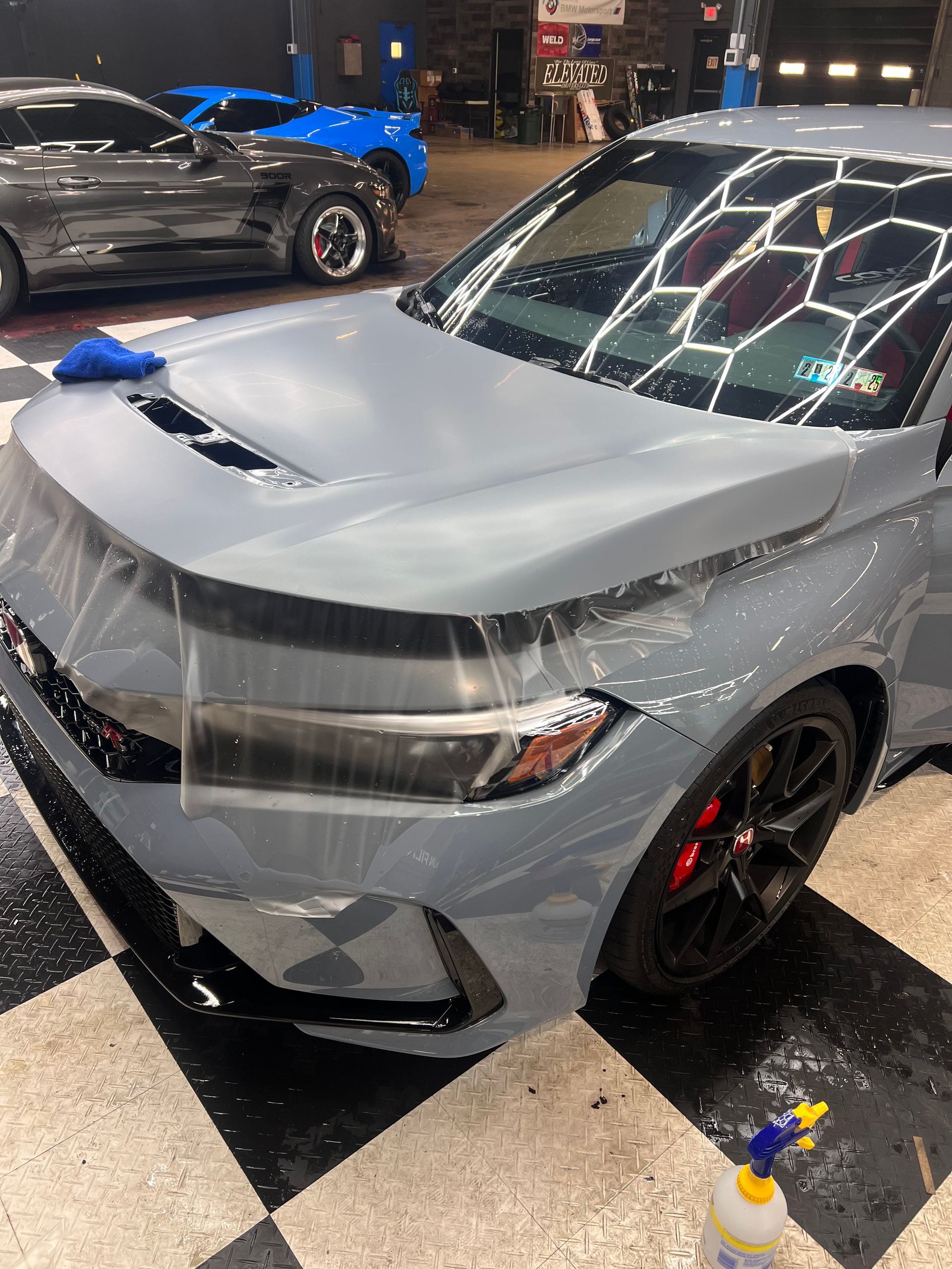 A car is wrapped in plastic and sitting on a checkered floor.