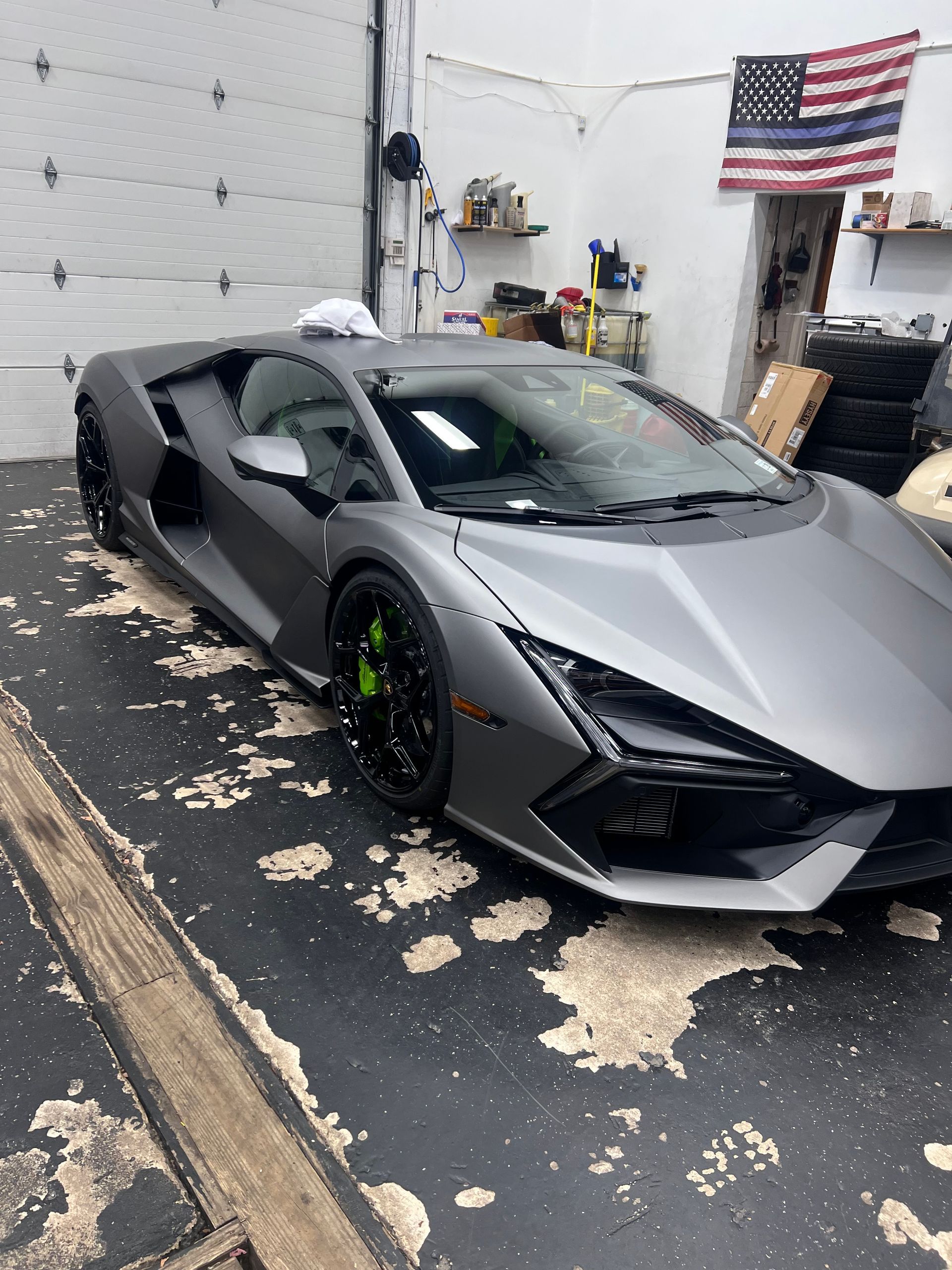 A gray sports car is parked in a garage next to an american flag