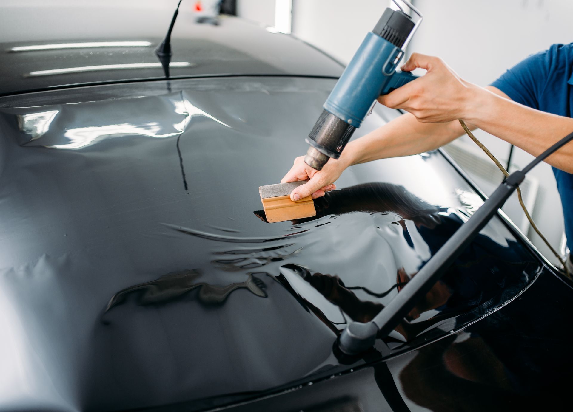 A man is applying window tinting to a black car.