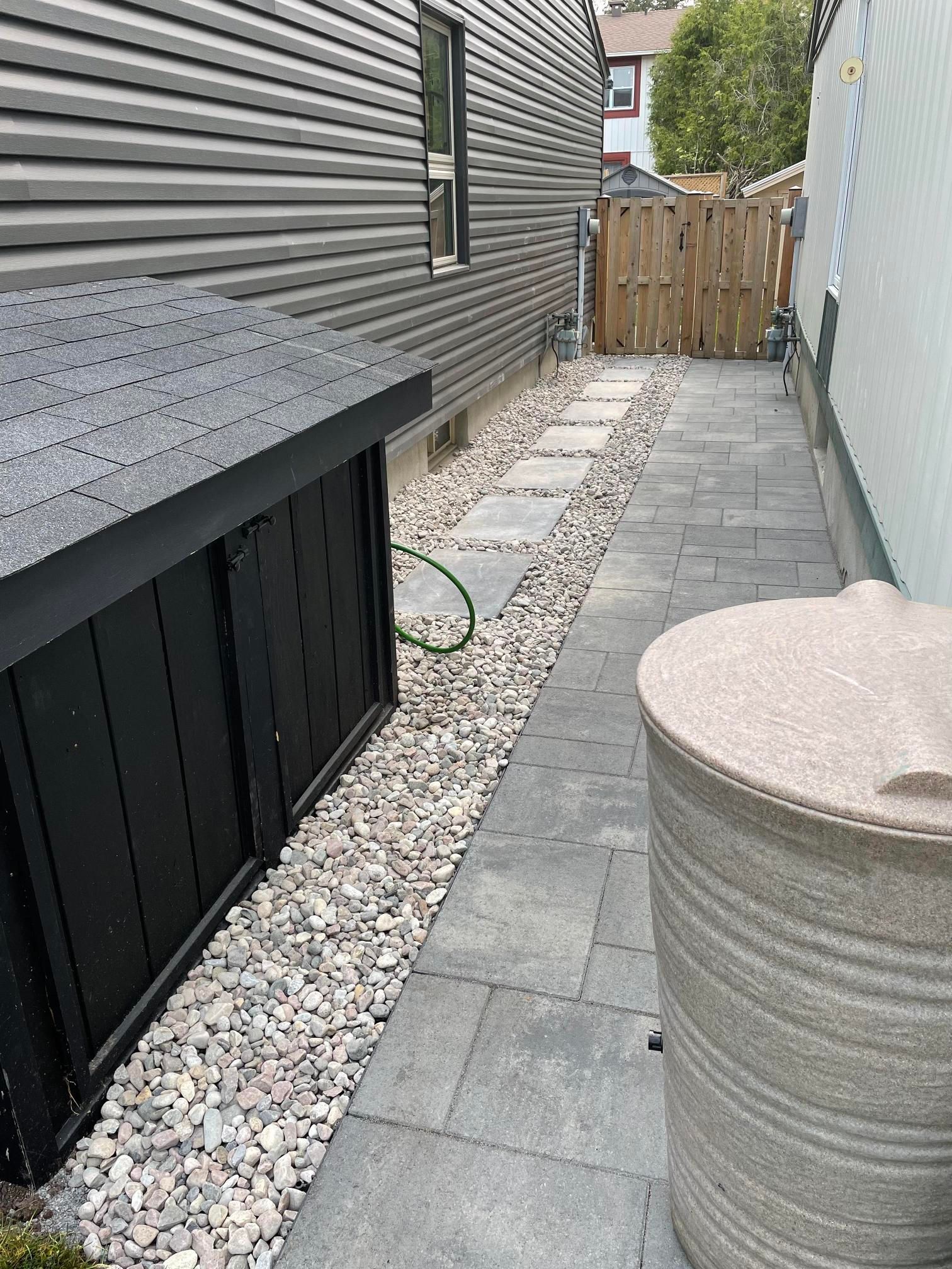 Une passerelle en pierre menant à une maison avec une clôture et un hangar noir.