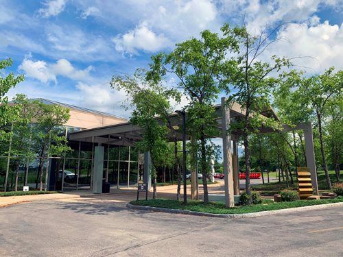 Building entrance with canopy, glass windows, and trees, under a blue sky with clouds.