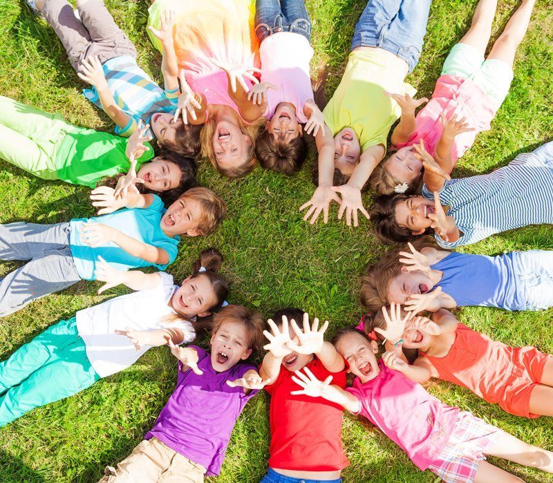 Children in a circle on grass, smiling and looking up, arms outstretched.