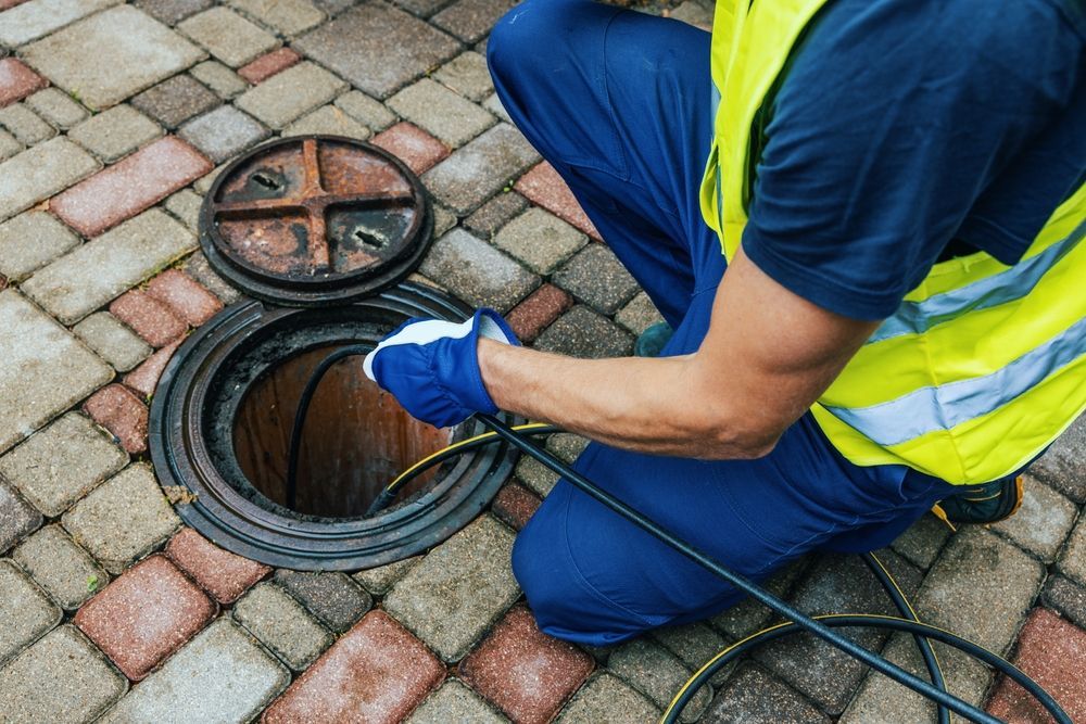 Person in Safety Vest Inspecting a Manhole in a Brick Paved Area — Hunter Plumbing And Hotwater in Raymond Terrace, NSW
