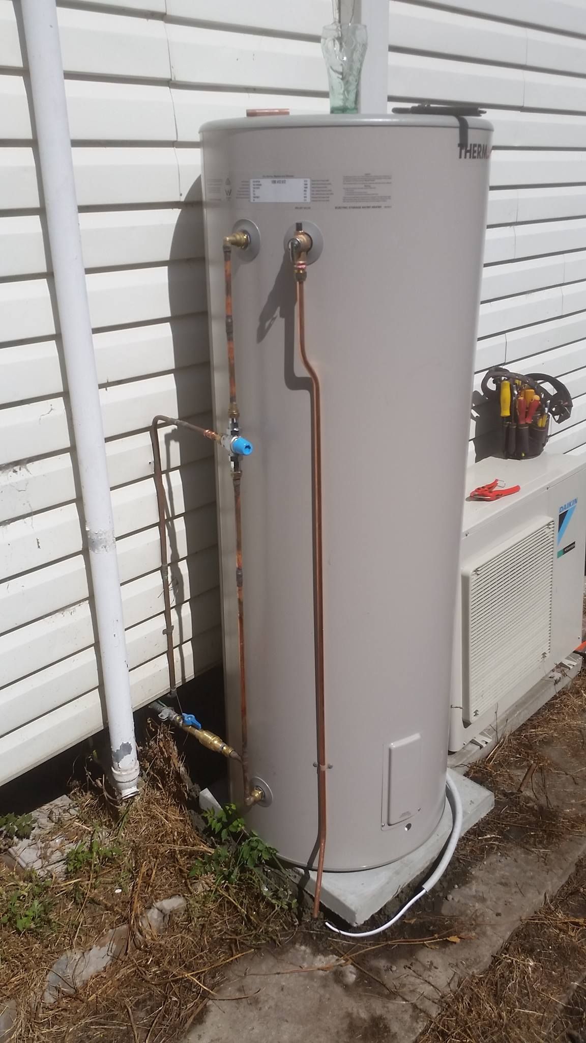 Hot Water Tank Against a White Building, With Copper Pipes and a Blue Valve — Hunter Plumbing And Hotwater in Medowie, NSW