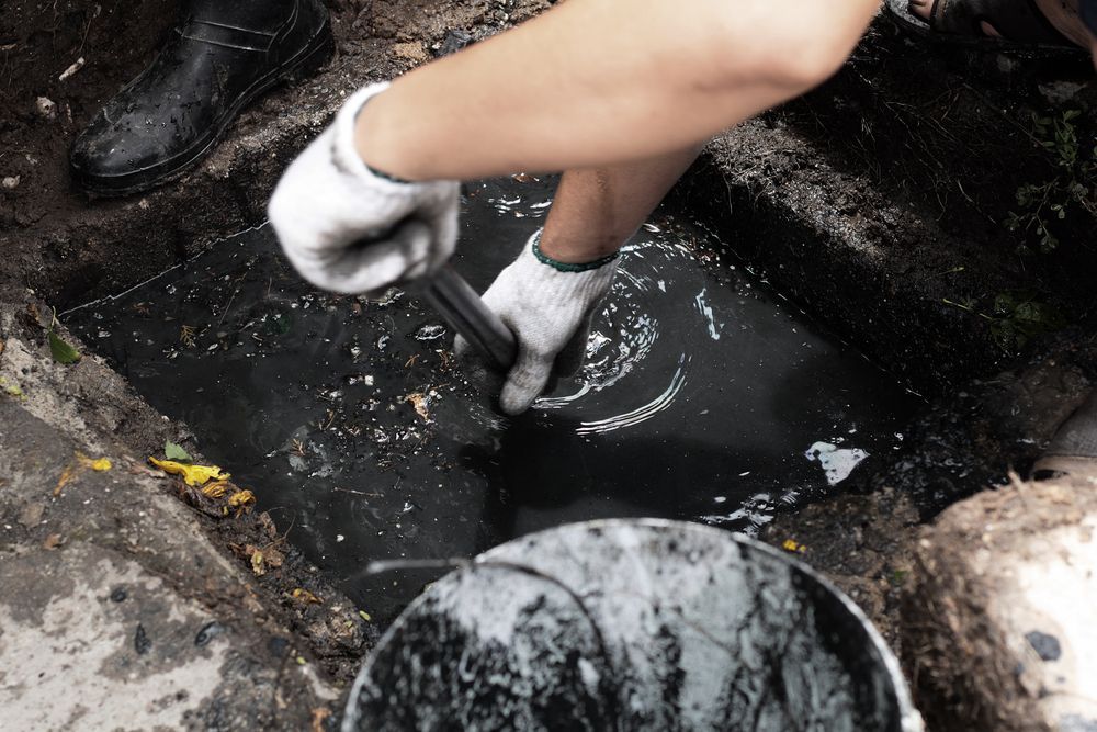 Person Using a Tool to Clean a Dark Liquid in a Drain — Hunter Plumbing And Hotwater in Raymond Terrace, NSW