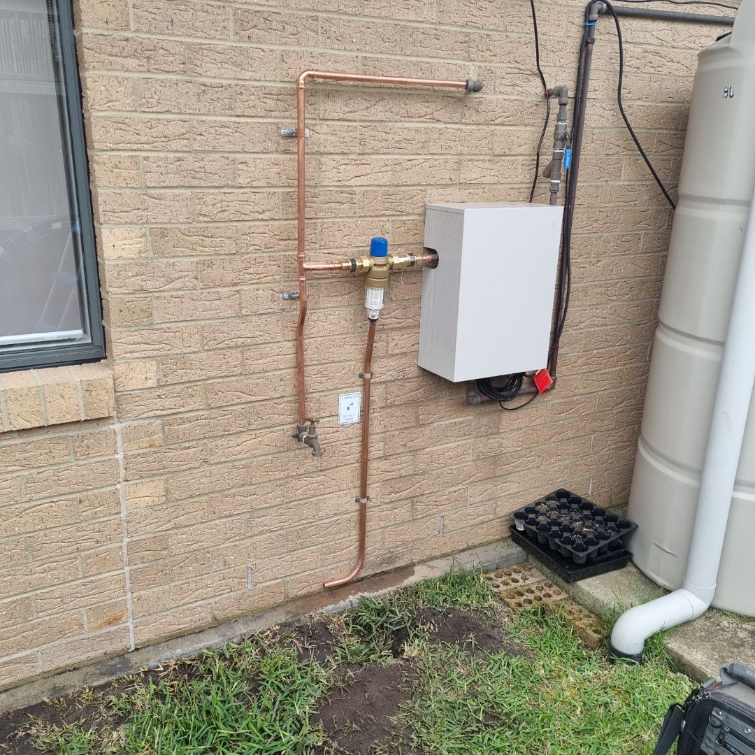 Copper Pipes and a White Water Heater Mounted on a Brick Wall — Hunter Plumbing And Hotwater in Port Stephens, NSW