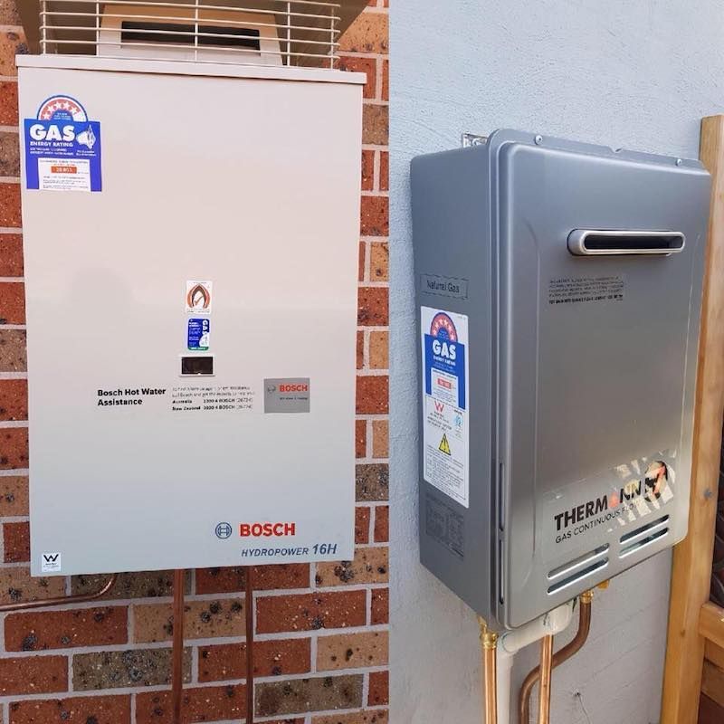 Two Wall-mounted Gas Water Heaters Side-by-side on Brick — Hunter Plumbing And Hotwater in Raymond Terrace, NSW