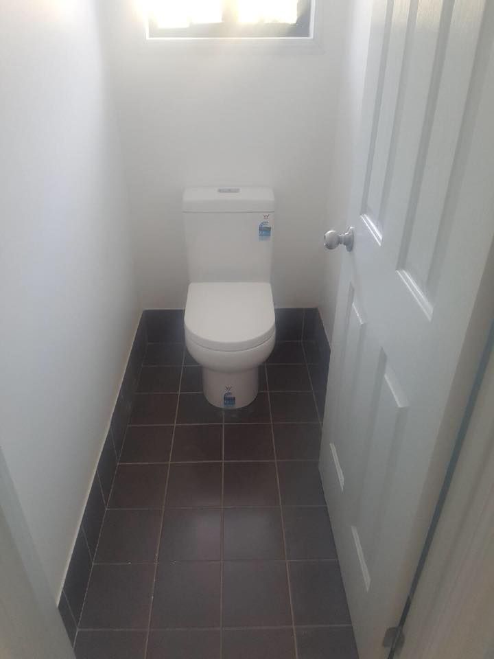 Small Bathroom With a White Toilet, Dark Brown Tiled Floor — Hunter Plumbing And Hotwater in Raymond Terrace, NSW