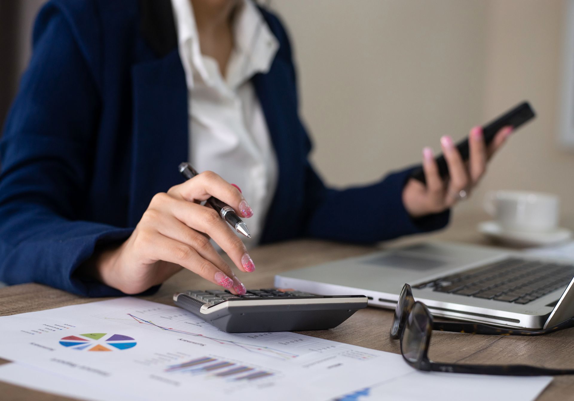 A woman is sitting at a desk using a calculator and a cell phone.
