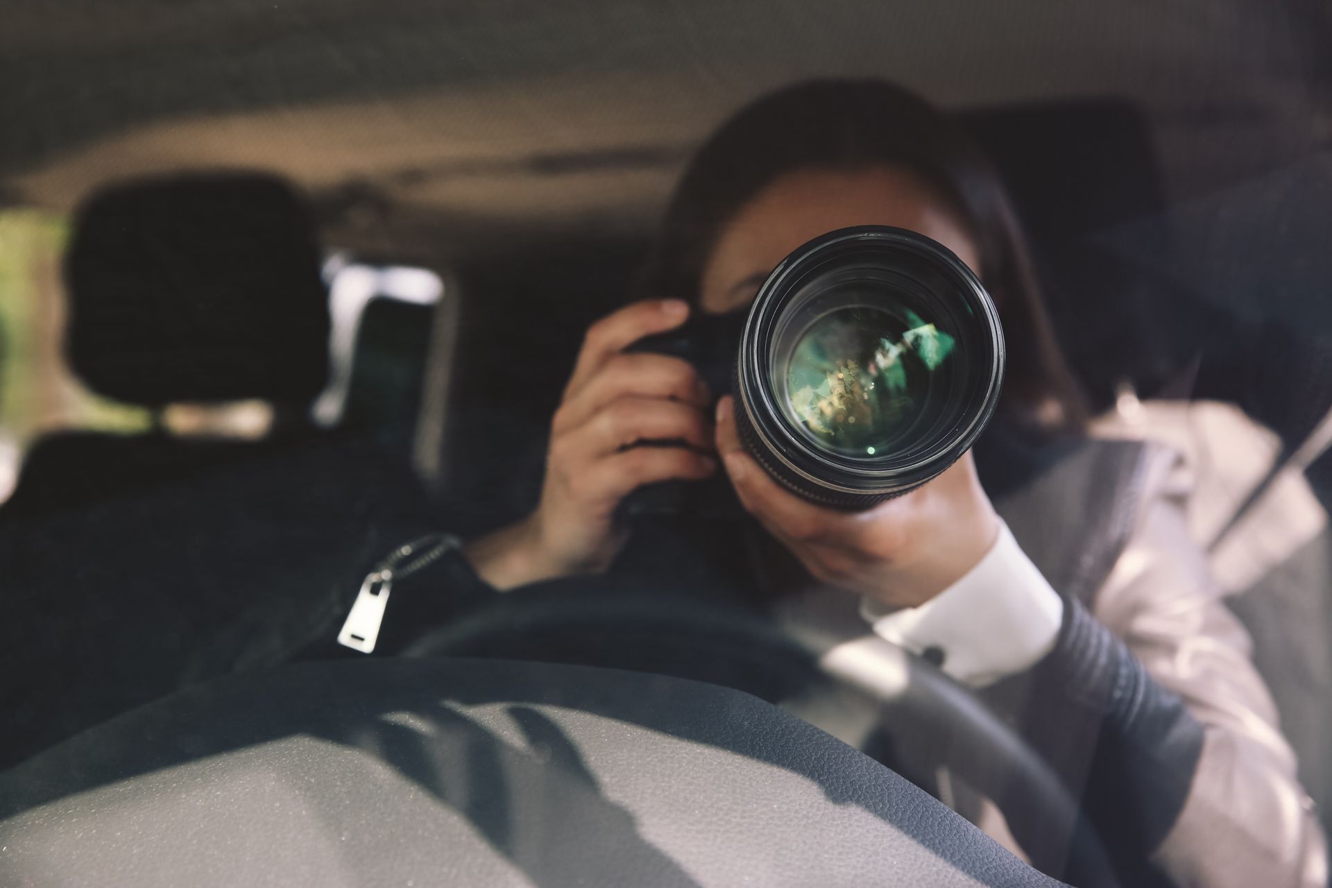 Private investigator conducting spouse surveillance from car using professional camera lens.