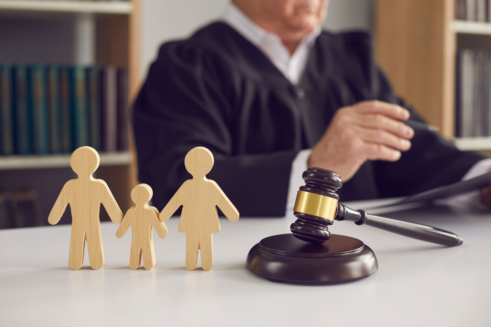 Wooden family figures and a gavel on a desk with a judge seated in the background.