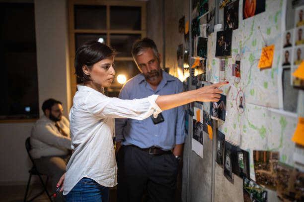 A woman is pointing at a bulletin board while a man looks on.