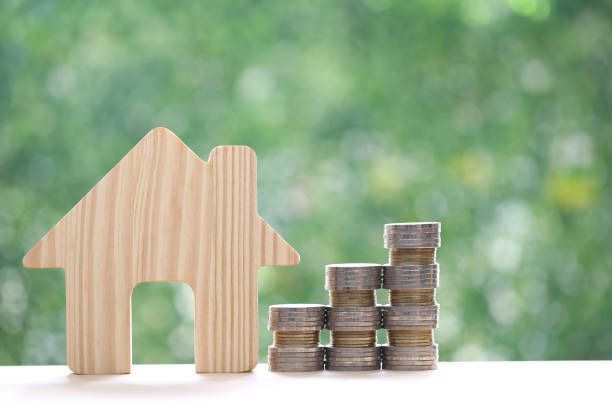 A wooden house and stacks of coins on a table.