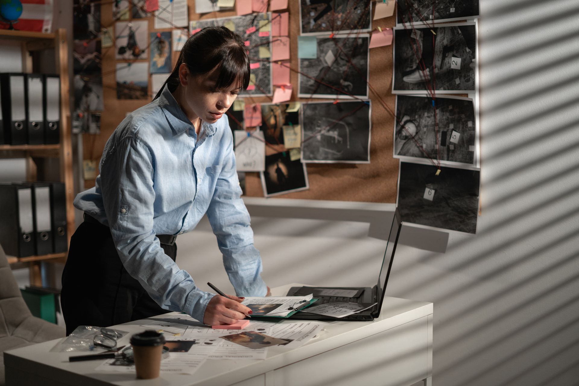 Female criminal investigator working at desk with laptop computer in her office.