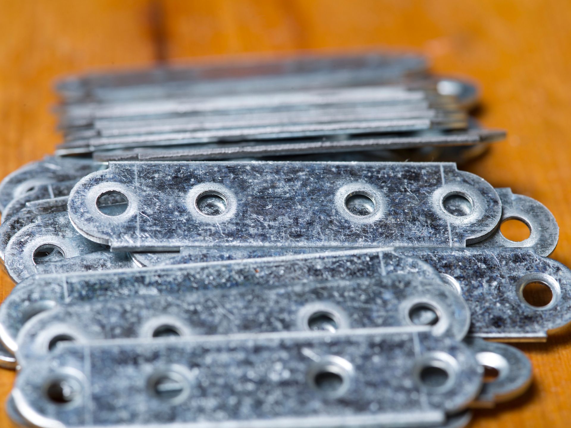Stacked galvanized steel brackets with holes on a wooden surface, ready for construction use.