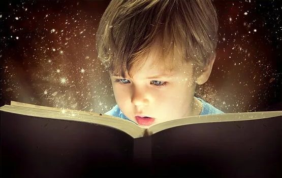 A young boy is reading a book with a light coming out of it.