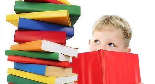 Boy peeking over a book at a large stack of books