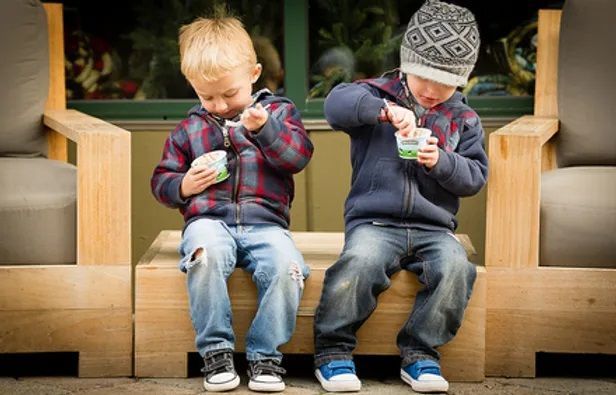 Two boys sitting on a bench eating ice cream out of cups