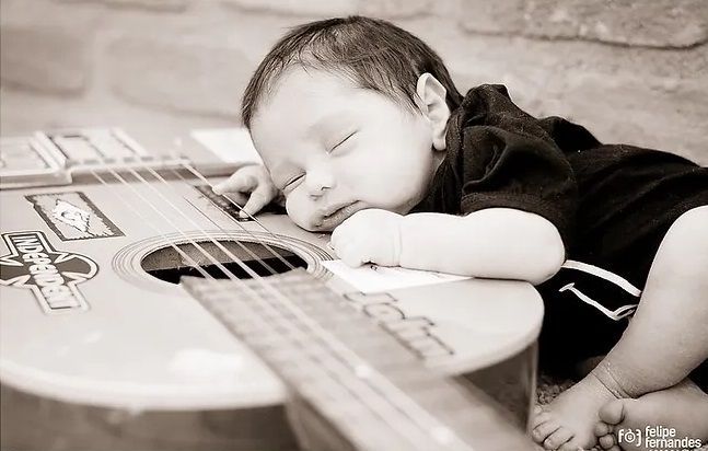 A baby is sleeping on top of an acoustic guitar