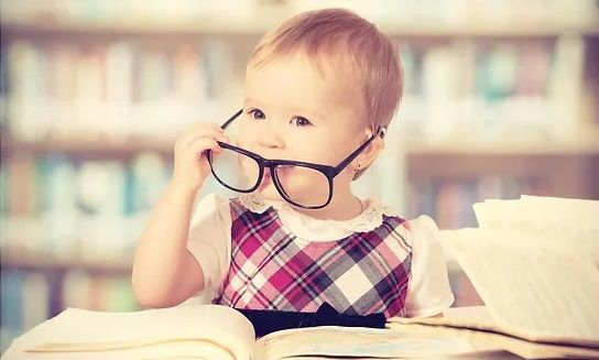 Child with adult sized glasses on looking at a book in a library