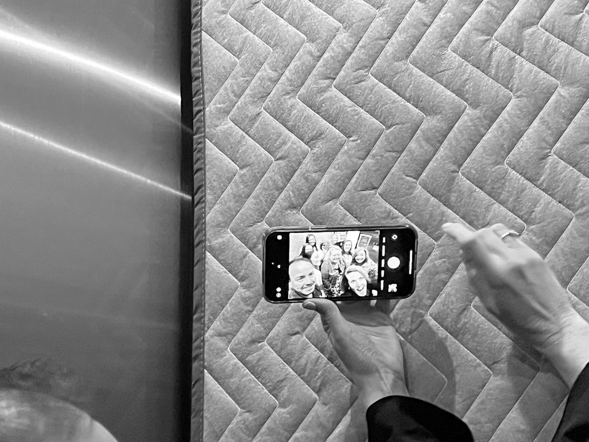 Person taking a selfie with a phone, angled slightly downwards, in front of a patterned wall.