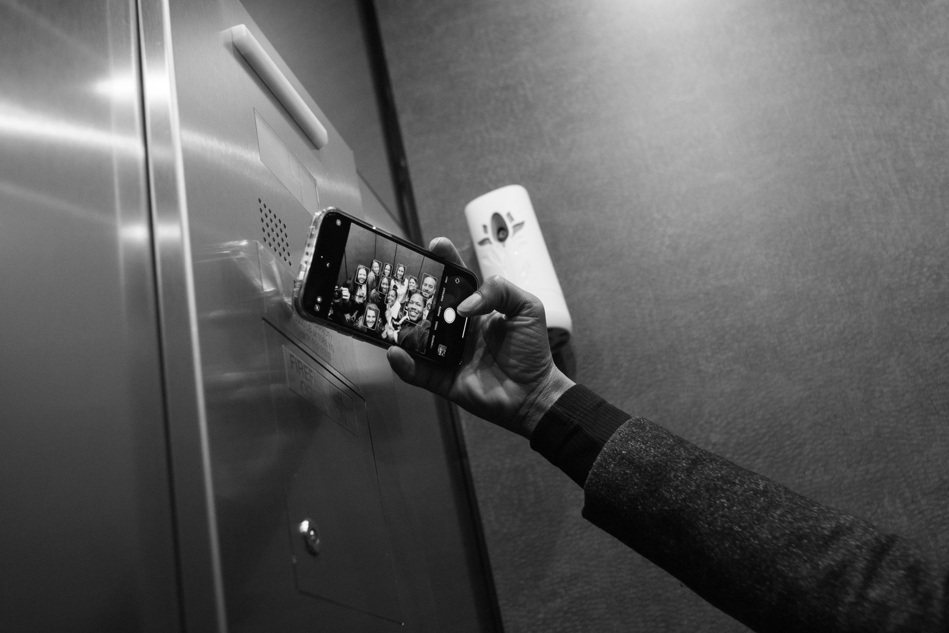 Person in a textured jacket takes a photo with a phone in an elevator.