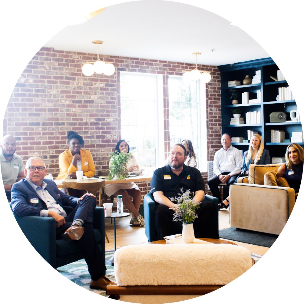 People in a room with brick wall, conversing, seated in chairs, and near a table.