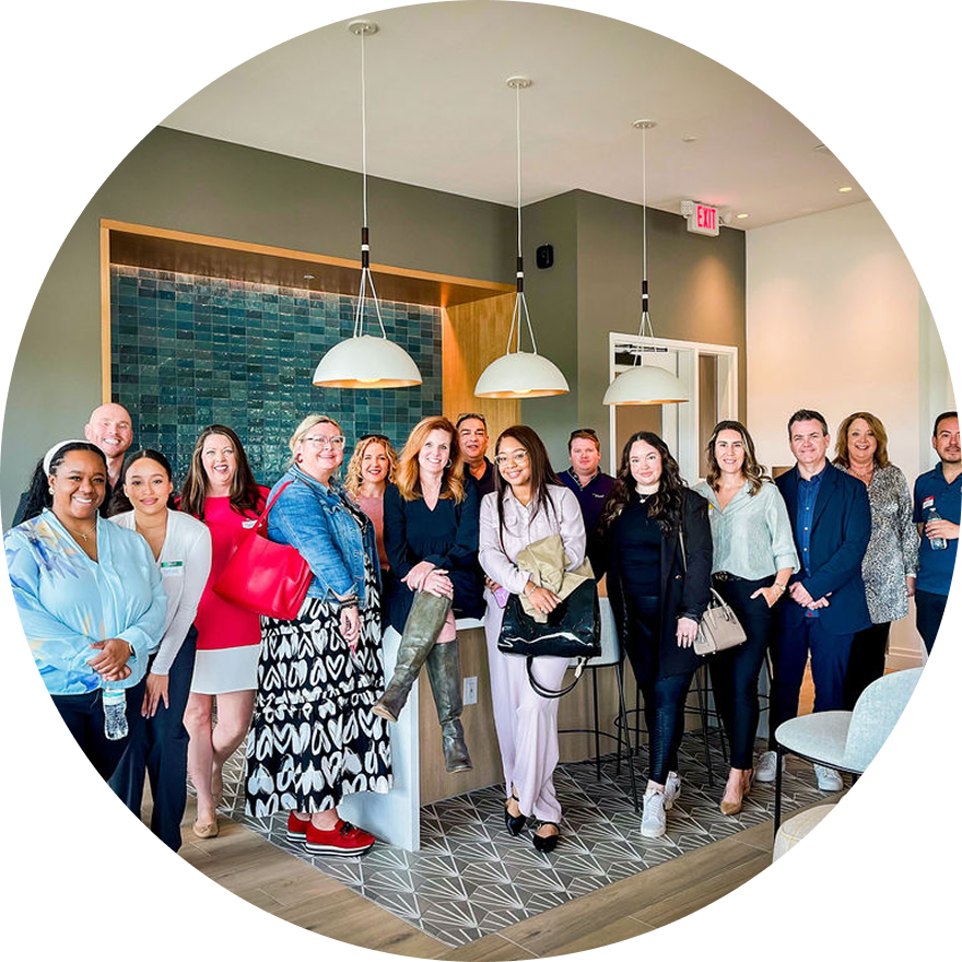 Group of people posing in a modern room with pendant lights, possibly an office or open house.