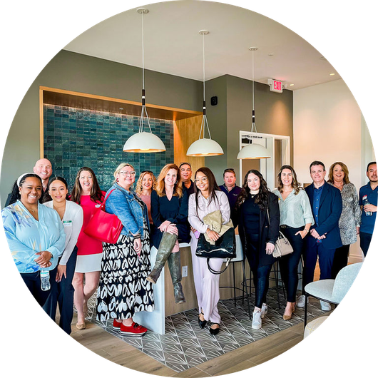Group of people posing in a modern room with pendant lights, possibly an office or open house.