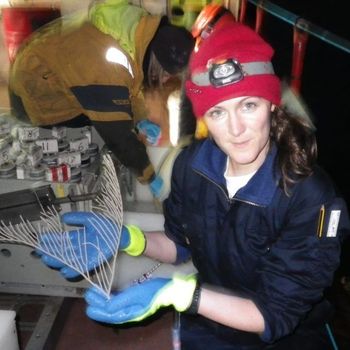 Woman on a boat holds a delicate, feathery, white sea creature, wearing a red hat and blue gloves.