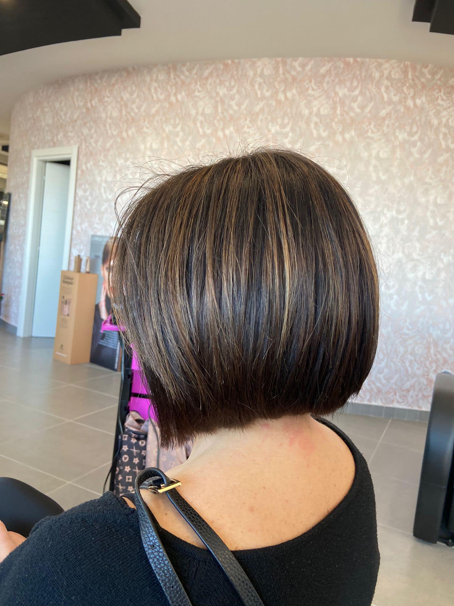 Una donna con i capelli castani corti è seduta su una sedia in un salone.