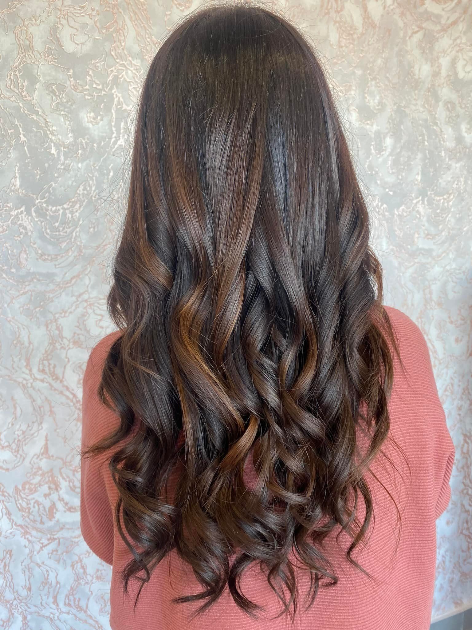 Una donna con lunghi capelli castani ricci indossa un maglione rosa.