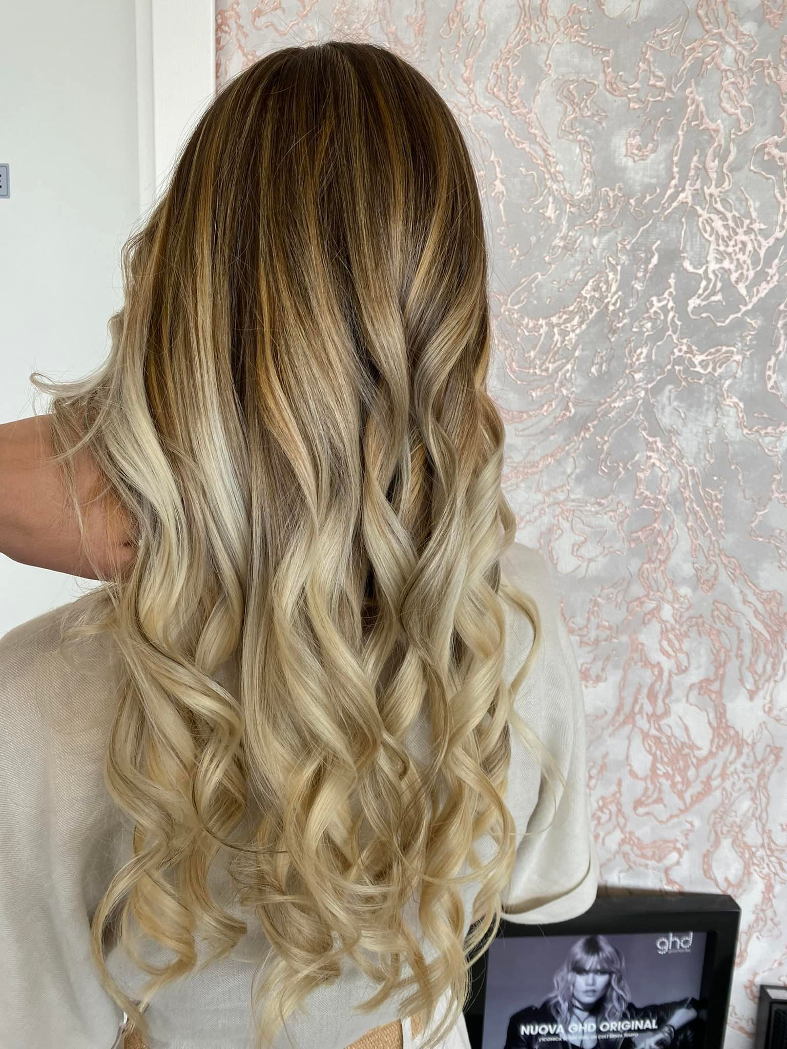 Una donna con lunghi capelli biondi si sta facendo sistemare i capelli dal parrucchiere.