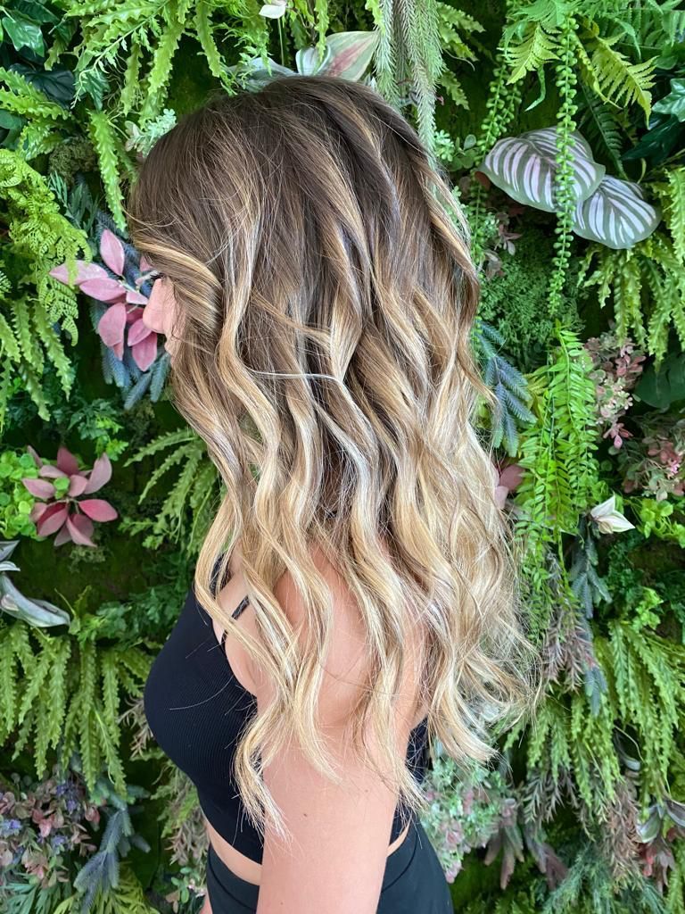 Una donna con lunghi capelli ondulati è in piedi davanti a un muro di felci.