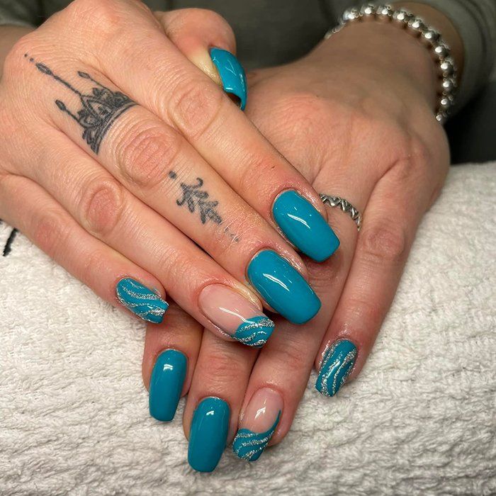 La mano di una donna con le unghie blu e un tatuaggio sul dito
